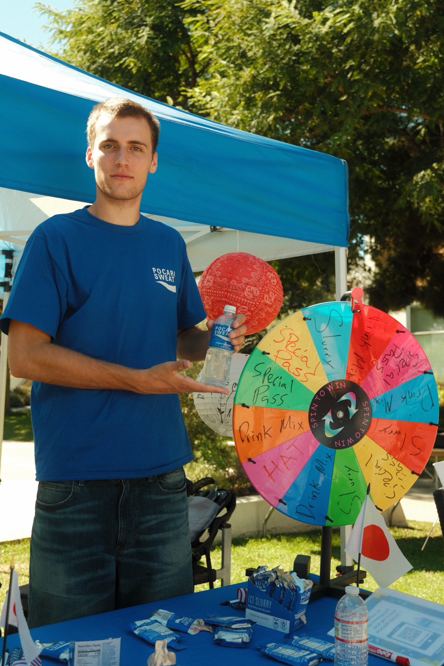 A staffer behind the Pocari Sweat table with the prize wheel and samples